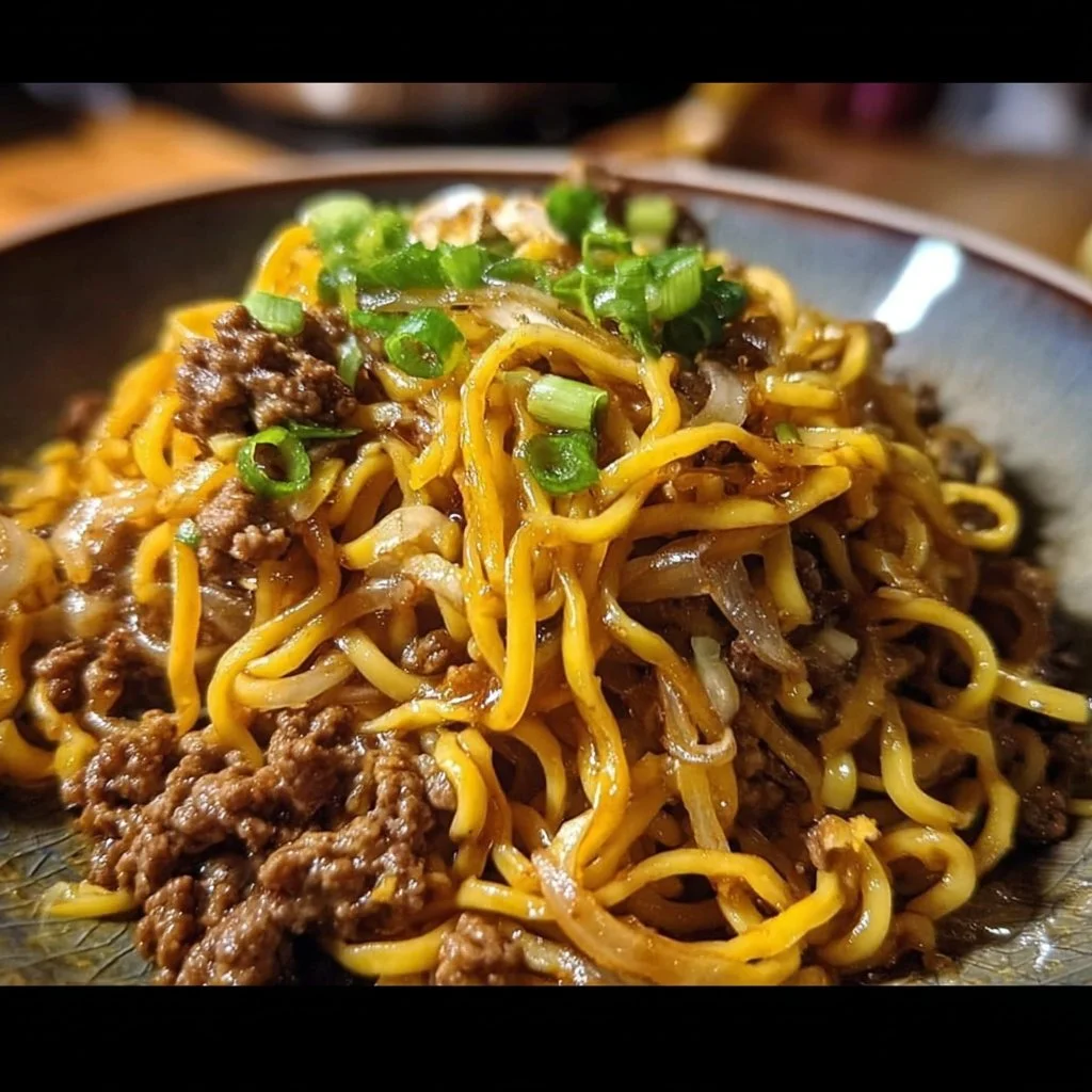 A plate of Mongolian ground beef noodles garnished with green onions.