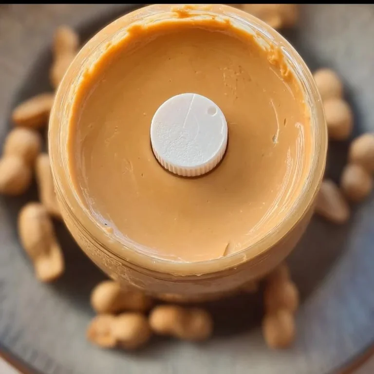 A jar of creamy homemade peanut butter with fresh peanuts and a spoon