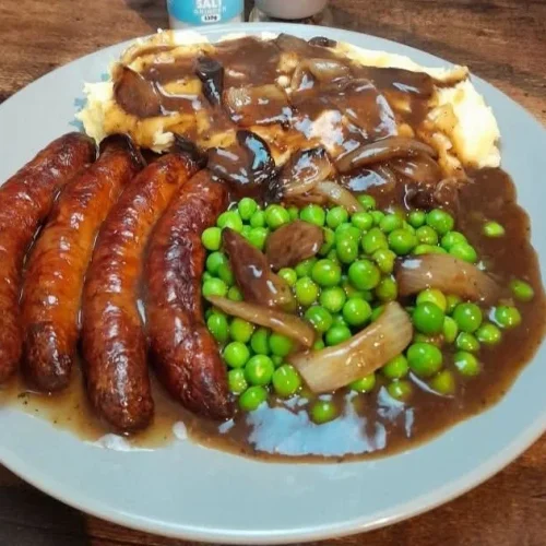 Tomato Sausages served with mash, peas, and savory meaty onion gravy
