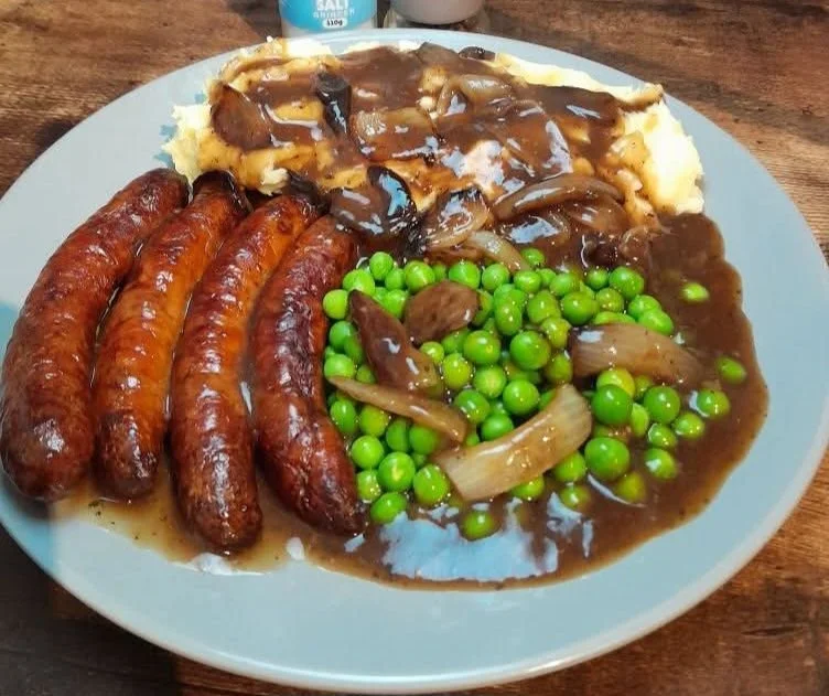Tomato Sausages served with mash, peas, and savory meaty onion gravy